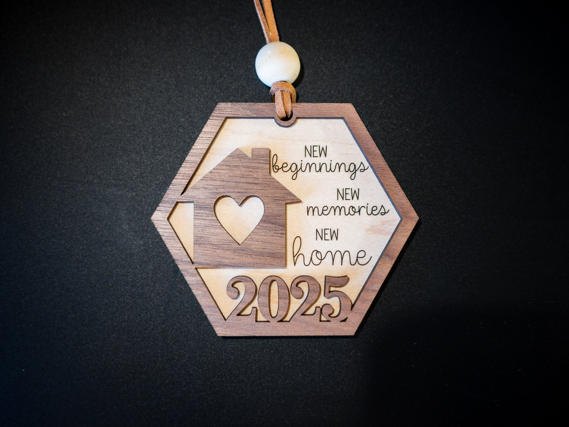 Wooden ornament with 'New beginnings, New memories, New home 2025' text on a dark background